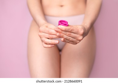 A Young Woman Folding A Pink Menstrual Cup In Her Hand. Pink Colored Background. Space For Text. Eco-friendly Silicone. Women's Health Cycle Mature Content. High Quality Photo