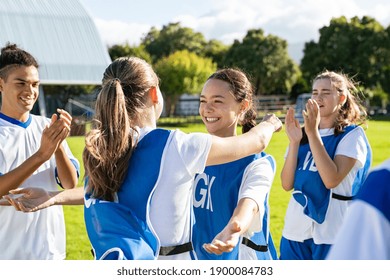 Young Woman Football Players Hugging With Open Arms After Goal. College Teammates Hugging And Celebrating Victory. Two Happy Friends Hugging On Soccer Field After Sport Match.