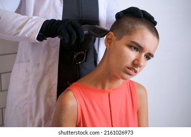 Young Woman Is Forcibly Shaving Her Head With An Electric Razor, Holding Typewriter In Black Gloves, A Girl With A Sad Look With Tears In Her Eyes. Close-up, Copy Space