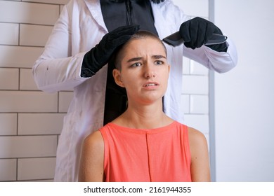 Young Woman Is Forcibly Shaving Her Head With An Electric Razor, Holding Typewriter In Black Gloves, A Girl With A Sad Look With Tears In Her Eyes. Close-up, Copy Space