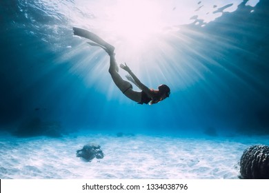 Young woman free diver glides over sandy sea with fins. Freediving in blue ocean - Shutterstock ID 1334038796