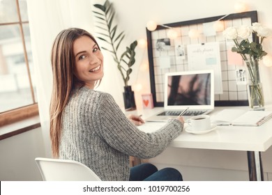 Young Woman Freelancer Indoors Home Office Concept Winter Atmosphere Sitting Writing In Planner Smiling