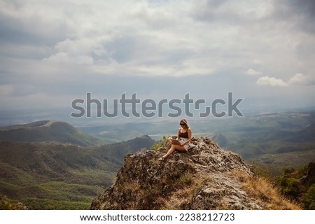 Young woman freelancer traveler working online anywhere outdoors using laptop enjoying mountain peak view. Happy female downshifter in sunglasses holding computer in unusual workplace at summer