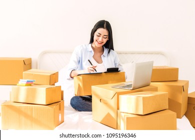 Young woman freelancer working and checklist and writing order with cardboard box on bed at home - SME business online and delivery concept