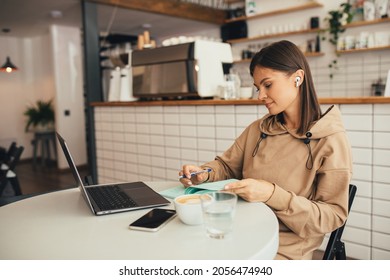 Young Woman Freelancer Working Online Using Her Laptop, Drinking Coffee In A Cozy Coffeehouse. Remote Work.