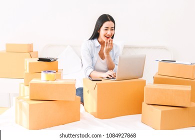 Young Woman Freelancer Working And Use Laptop Computer With Cardboard Box On Bed At Home - SME Business Online And Delivery Concept