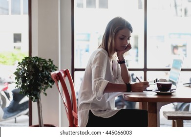 Young Woman Freelancer Writing Notes In Cafe