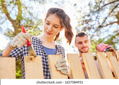 Young woman and friend together in priming and varnishing wooden fence in the garden