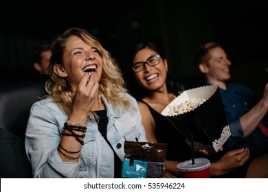Young woman with friends watching movie in cinema and laughing. Group of people in theater with popcorns and drinks.