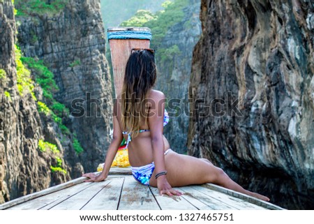 Young woman at the front bow of a longtail boat with the rocky cliffs in the front. Woman on bikini during vacation in Thailand.