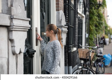 Young Woman In Front Of Entrance Door, Ringing At The Door Bell