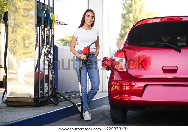 Young woman with fuel pump nozzle near car at\
self service gas station