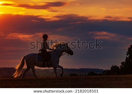 young woman galloping on horse during sunset
