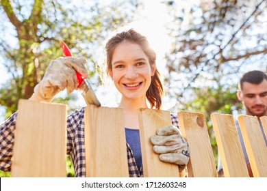 Young Woman In Garden With Brush At Fence Paint With Wood Paint As Home Improvement