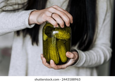 A young woman, a gardener, a cook, holds a glass jar with canned cucumbers, preserves, in her hands in the kitchen, opening the lid. Food photography. - Powered by Shutterstock