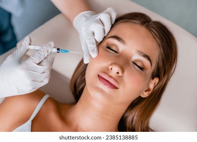 Young woman gets beauty facial injections in salon. Treatment, facial anti-age procedures. Cosmetologist hands in gloves doing shots with syringe - Powered by Shutterstock