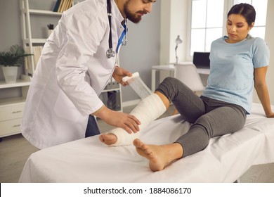 Young Woman Gets First Aid At The Hospital After An Accident. Medical Specialist, Injury Care Center Traumatologist Or Orthopedic Surgeon Helps Female Patient And Applies Plaster Bandage On Broken Leg