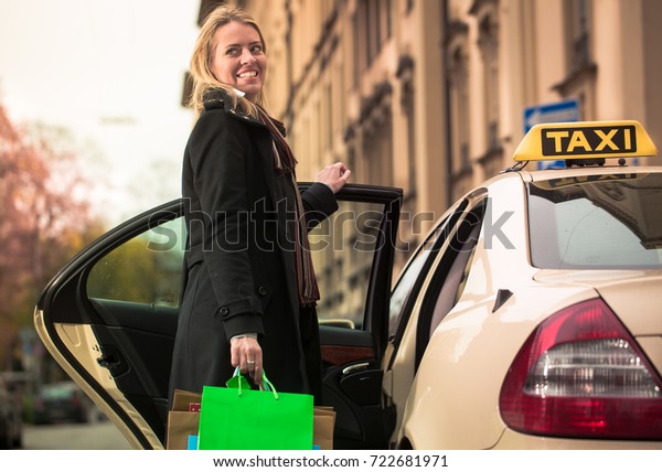 Young woman gets out of taxi carrying shopping bags\
in hands