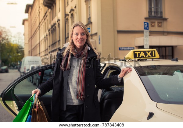 Young woman gets out of taxi carrying shopping bags\
in hands