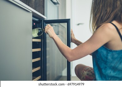 A young woman is getting a bottle of white wine from her wine cooler at home