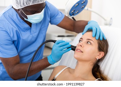 Young Woman Getting Facial Electroporation Procedure From Experienced Male Cosmetologist In Aesthetic Medicine Office