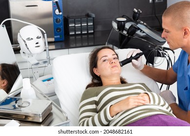 Young Woman Getting Facial Electroporation Procedure From Experienced Male Cosmetologist In Aesthetic Medicine Office