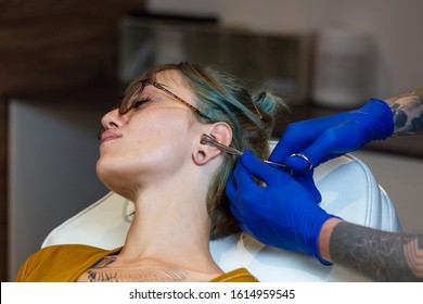 Young Woman getting her ear pierced. Man showing a process of piercing with sterile medical equipment and latex gloves. Body Piercing Procedure. Beautiful woman getting her ear pierced