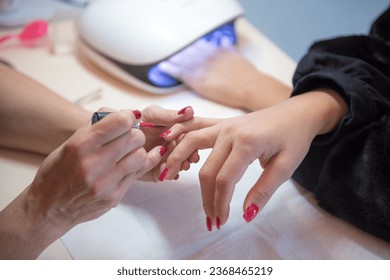 young woman getting a manicure applying semi-permanent nail polish and with an ultraviolet lamp in a beauty salon