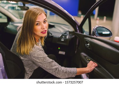 Young Woman Getting Out Of The Parked Car Looking To The Camera Smiling On The Parking In The City At Night