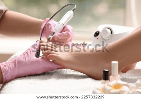 Young woman getting pedicure with milling cutter in beauty salon, closeup