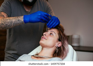 Young Woman getting pierced between her eyes. Man showing a process of piercing with steril medical equipment and latex gloves. Body Piercing Procedure