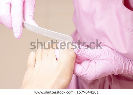 Young woman getting professional pedicure in a beauty salon, closeup. Hands a pedicurist in protective rubber gloves are applied with nails to the nails using a nail file. Pedicure, manicure concept