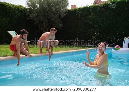 Young woman getting splashed by friends from outside of a swimming pool.