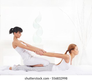 Young woman getting traditional Thai stretching massage by therapist over spa salon background