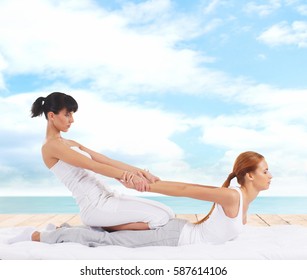 Young woman getting traditional Thai stretching massage by therapist on a pier