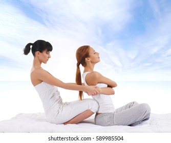 Young woman getting traditional Thai stretching massage by therapist over sky background
