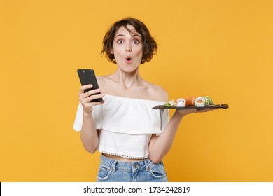 Young Woman Girl In Casual Clothes Hold In Hand Makizushi Sushi Roll Served On Black Plate Japanese Food Using Mobile Cell Phone Isolated On Yellow Background Studio Portrait People Lifestyle Concept