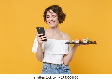 Young Woman Girl In Casual Clothes Hold In Hand Makizushi Sushi Roll Served On Black Plate Japanese Food Using Mobile Cell Phone Isolated On Yellow Background Studio Portrait People Lifestyle Concept