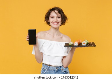 Young Woman Girl In Casual Clothes Hold In Hand Makizushi Sushi Roll Served On Black Plate Japanese Food Using Mobile Cell Phone Isolated On Yellow Background Studio Portrait People Lifestyle Concept