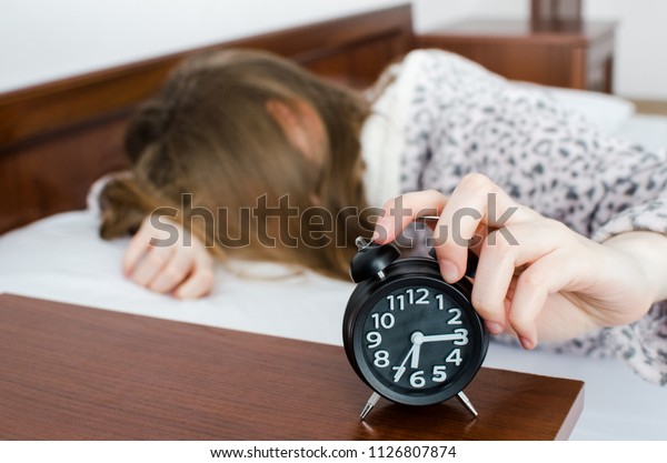 Young woman girl turns off alarm clock waking up\
in the morning from a call. Unrecognizable student do not want to\
wake up early for school or univercity. Oversleep, not getting\
enough sleep concept.