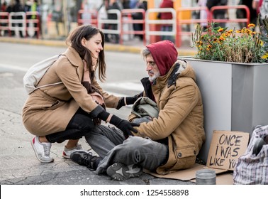 Young woman giving money to homeless beggar man sitting in city.
