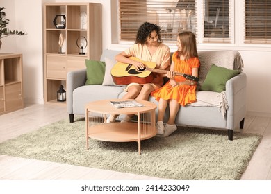 Young woman giving music lessons to teenage  girl with acoustic guitar at home - Powered by Shutterstock