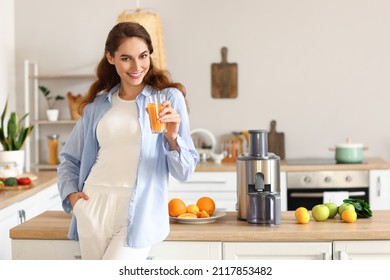 Young woman with glass of fresh fruit juice near modern juicer in kitchen