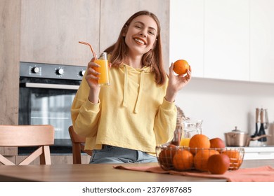 Young woman with glass of juice and orange in kitchen - Powered by Shutterstock