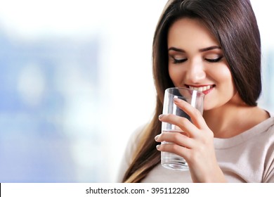 Young woman with a glass of water sitting on sofa in the room - Shutterstock ID 395112280