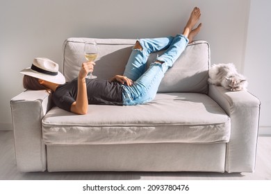 Young woman with glass of white wine resting on the sofa at home. Woman enjoying free time and lazy weekend.