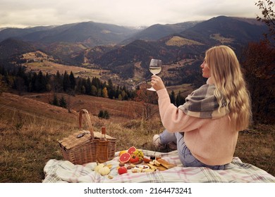 Young woman with glass of wine having picnic in mountains on autumn day - Powered by Shutterstock