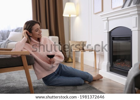 Young woman with glass of wine resting near fireplace at home