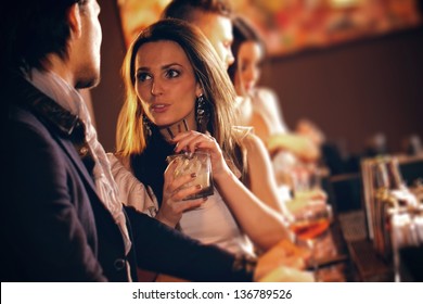 Young woman with a glass of wine talking to a man at the bar