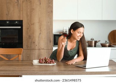 Young woman with glass of wine video chatting in kitchen - Powered by Shutterstock